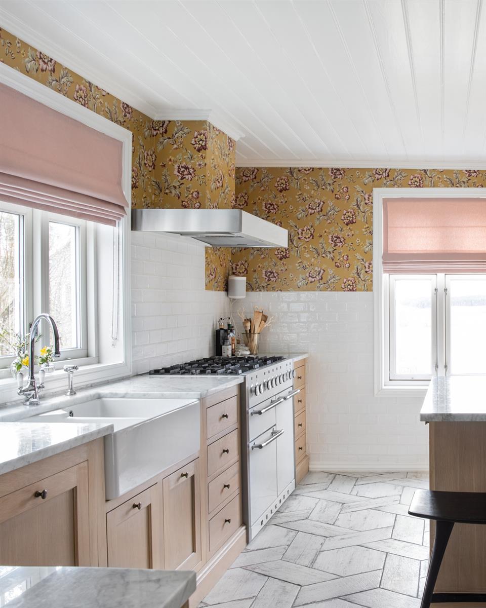 Kjøkken med liftgardin rosa, mønstret tapet og kjøkkeninnredning i tre. Foto.